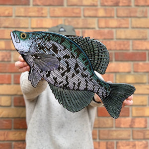 Person holding a detailed fish-shaped object against a brick wall.