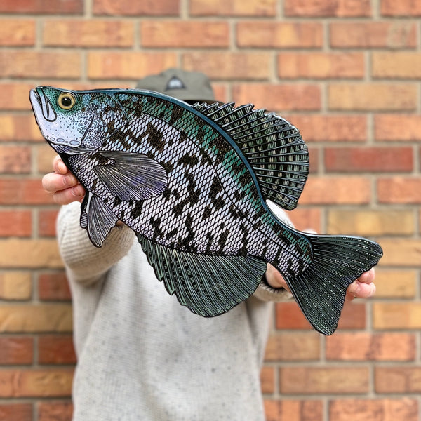 Person holding a detailed fish-shaped object against a brick wall.