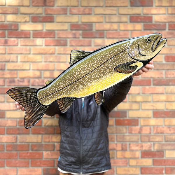 Person holding a large fish cutout against a brick wall